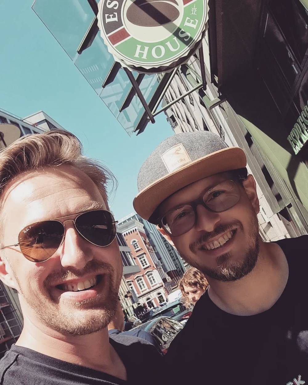 Two men smiling in a selfie in front of a pub sign reading "House."