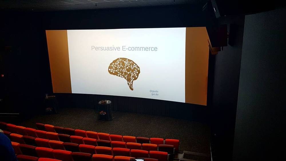 An empty cinema auditorium with a presentation slide reading "Persuasive E-commerce" on the big screen.