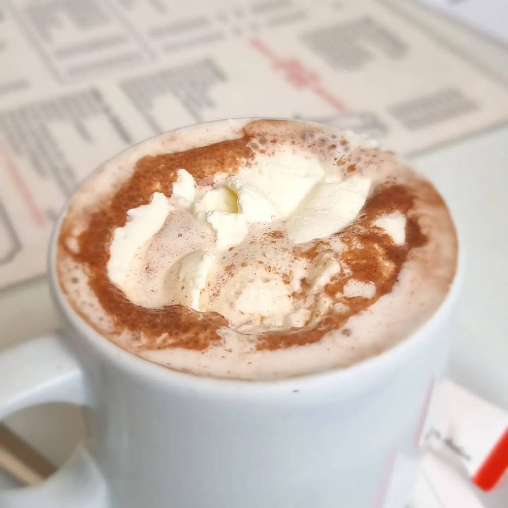 An overhead view of a cappuccino topped with whipped cream and cocoa powder, resting on a newspaper.