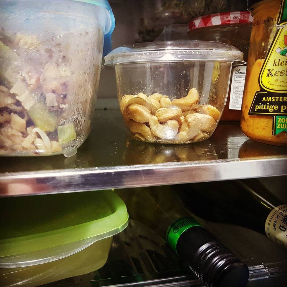 Leftover food containers, including cashews and a jar of peppers, on a fridge shelf.