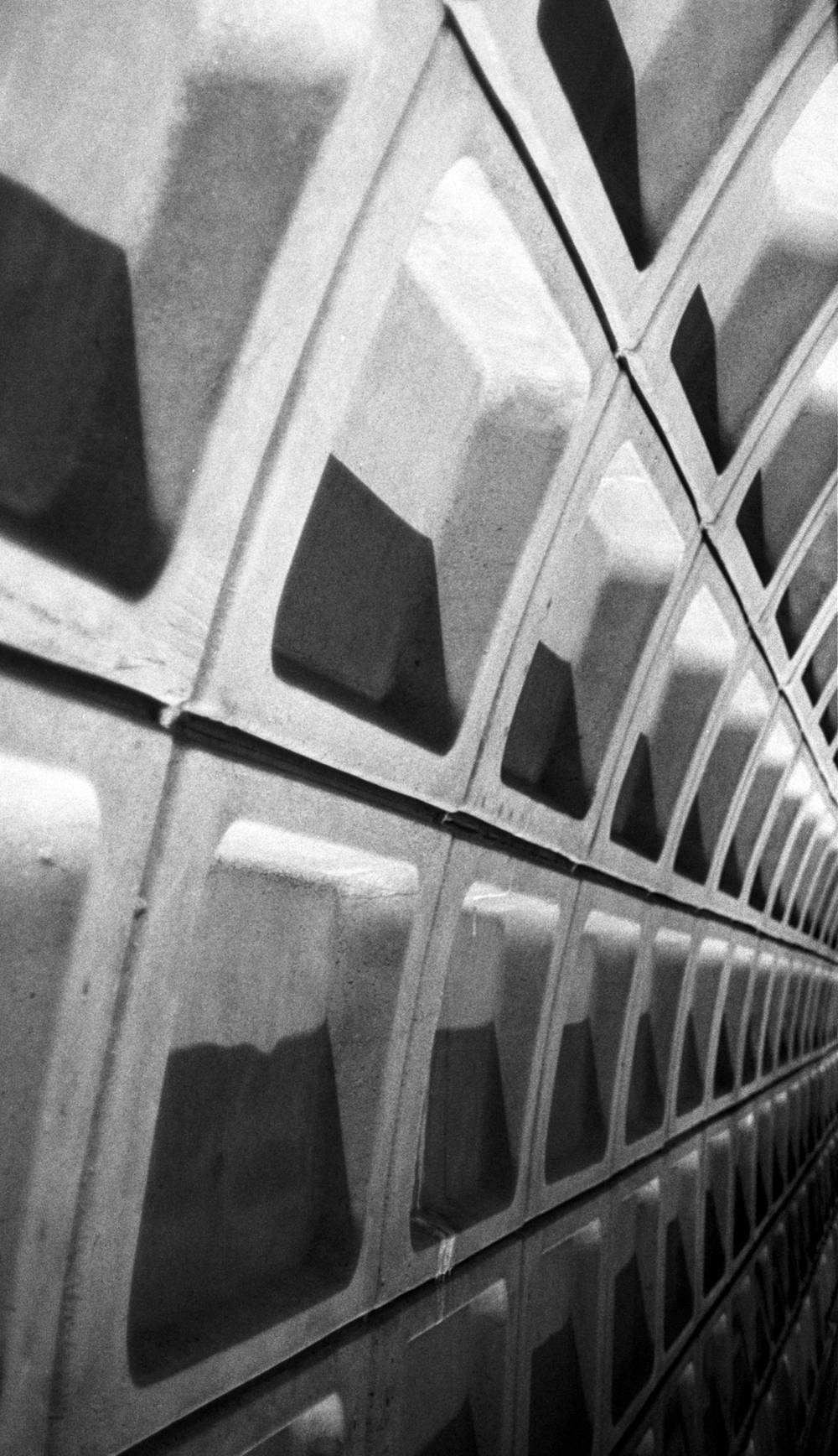 A repeating pattern of concrete block tiles set at an angle, featuring deep square indentations with sharp light and shadows.