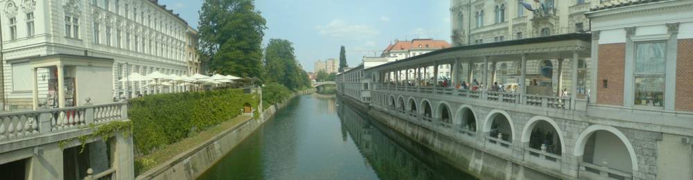 Cafe terraces and colorful buildings line a canal in Ljubljana's old town.
