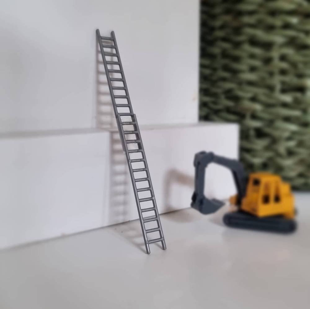 A toy excavator and a small ladder set up against a wall in a miniature construction scene.