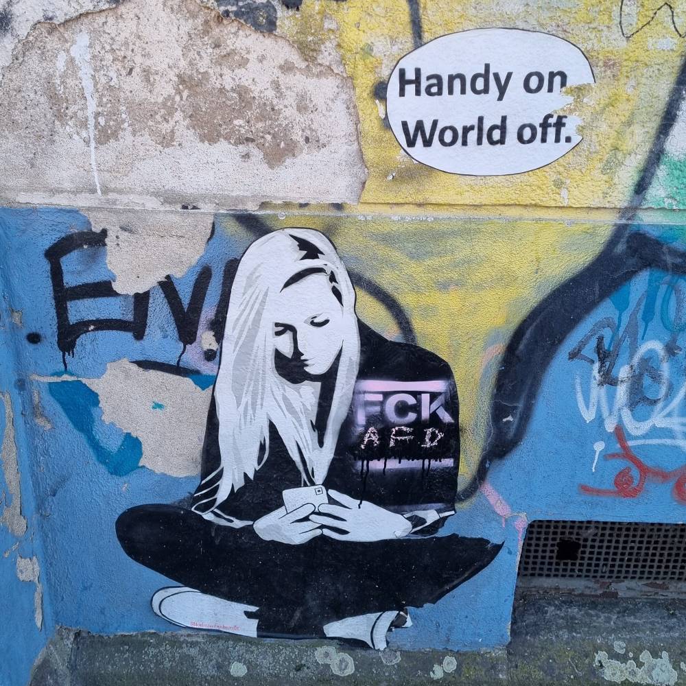 Woman sitting on a floor, scrolling her smartphone. In the right hand corner above a bubble, which reads "handy on, world off". 