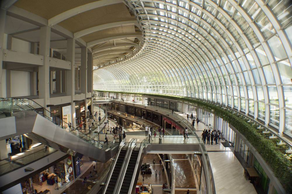 The curving glass roof of a shopping mall arcade, with escalators below.