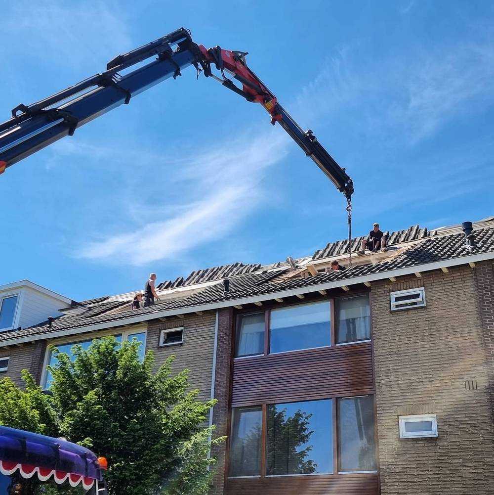 A crane lifting materials up to workers on a rooftop under construction.