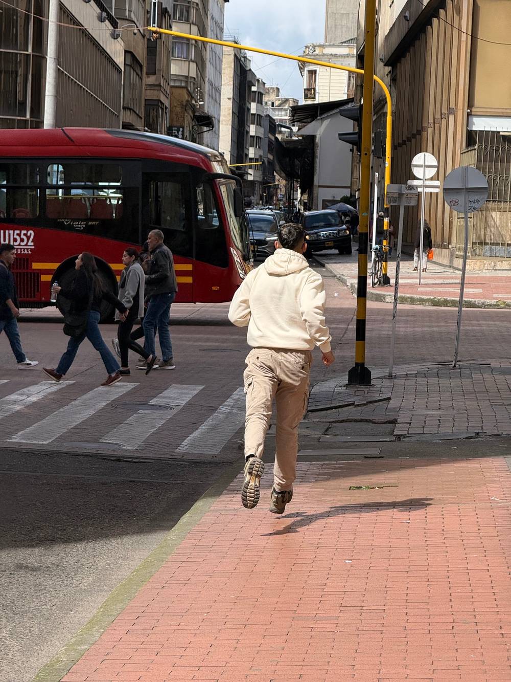 A man races down the street, seemingly towards a bus, with people walking in the mid-ground