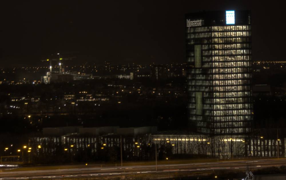 The same illuminated tower is seen from a different angle above city lights at night.