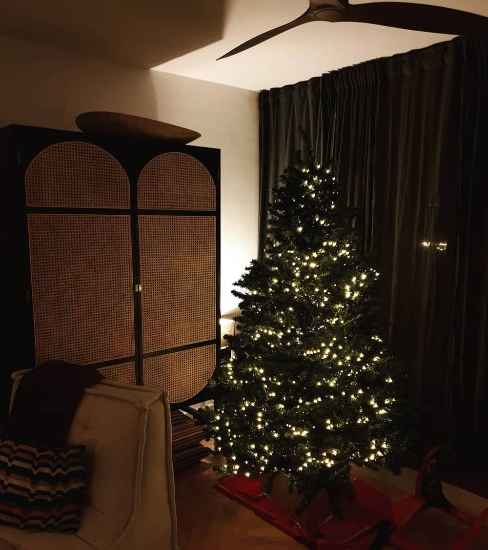 A cozy living room corner with a decorative folding screen beside a Christmas tree strung with warm lights.