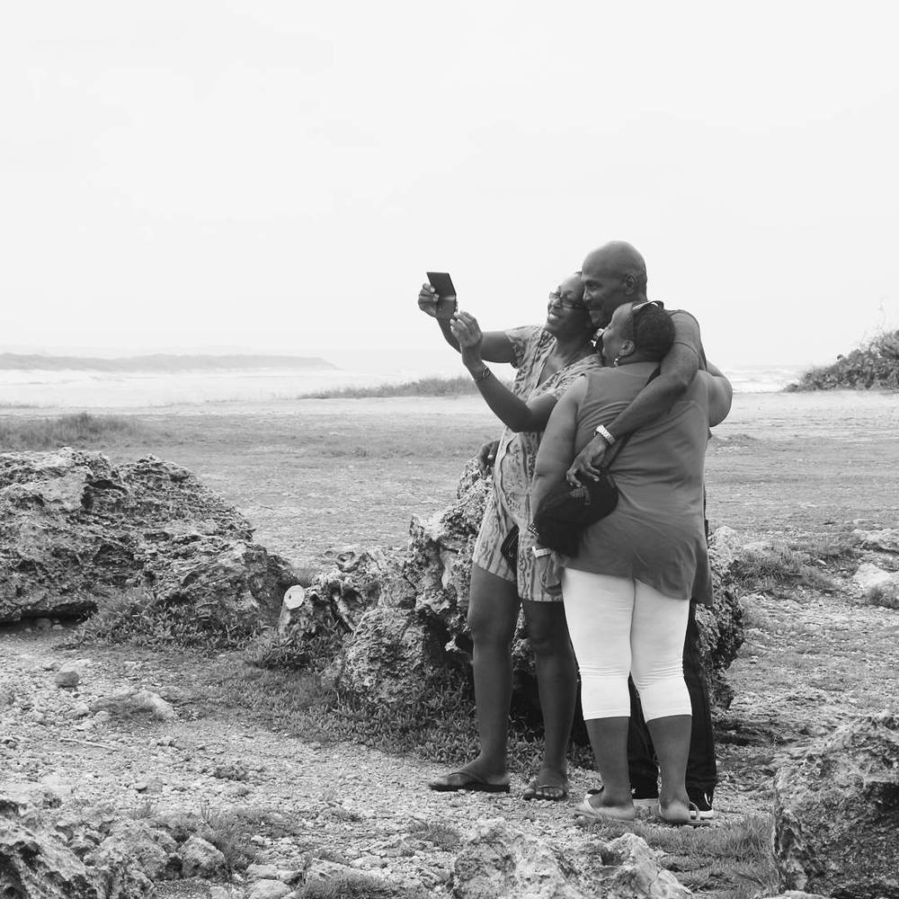 Black and white photo of a family taking a selfie on rocks by the coast.