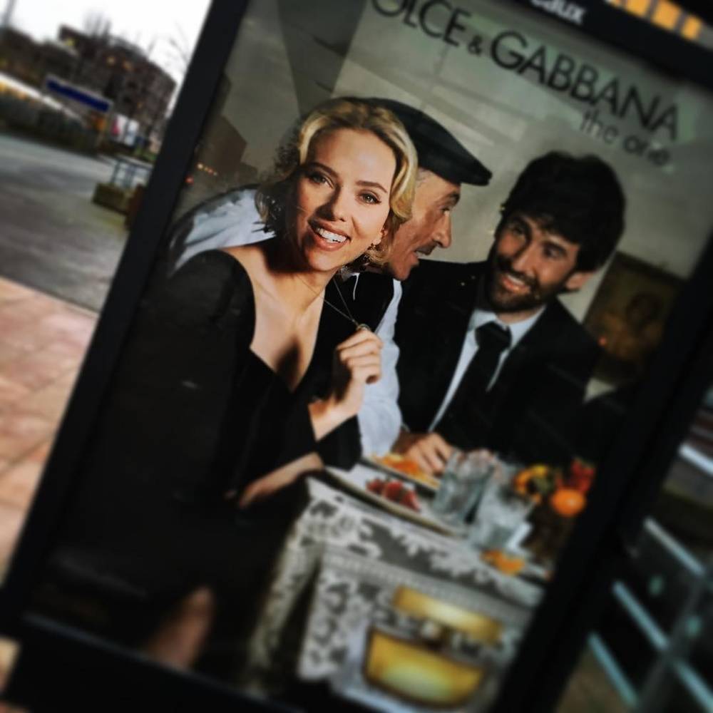 A bus shelter advertisement featuring a Dolce & Gabbana campaign image of a family at a table.