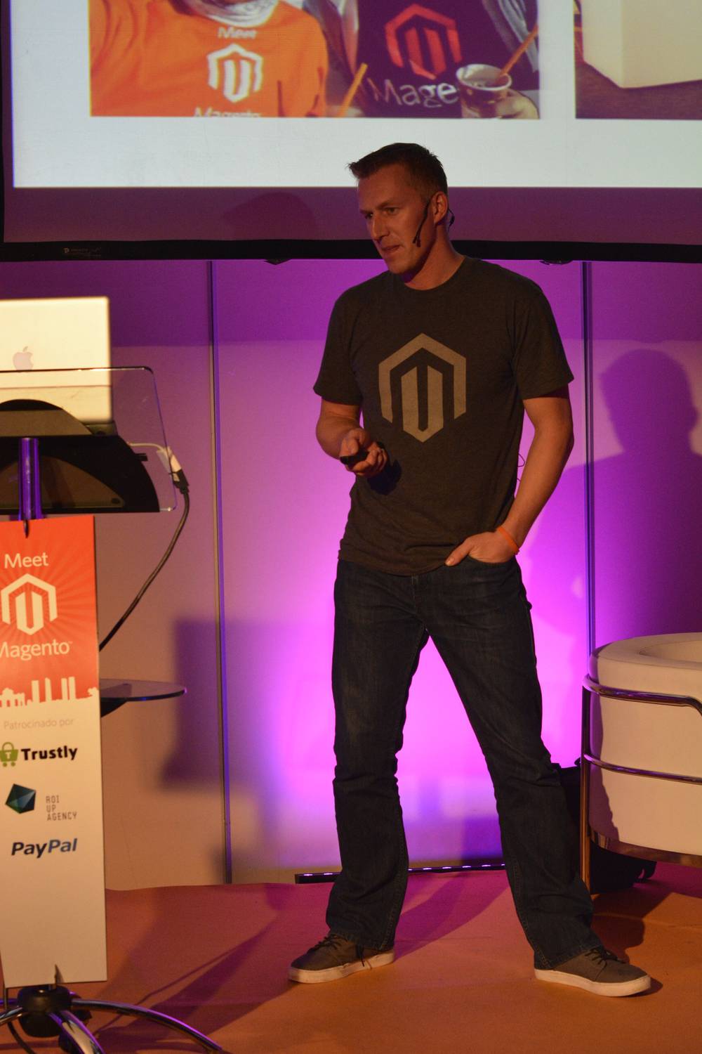 A man in a Magento t-shirt presents on stage under purple lighting.