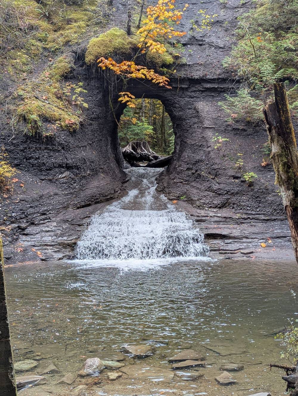A small waterfall flowing through an almost circular hole in a rock wall. Hole in the Wall. On Vancouver Island, BC