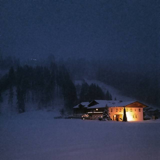 A chalet lit up at night in a snowy alpine landscape.