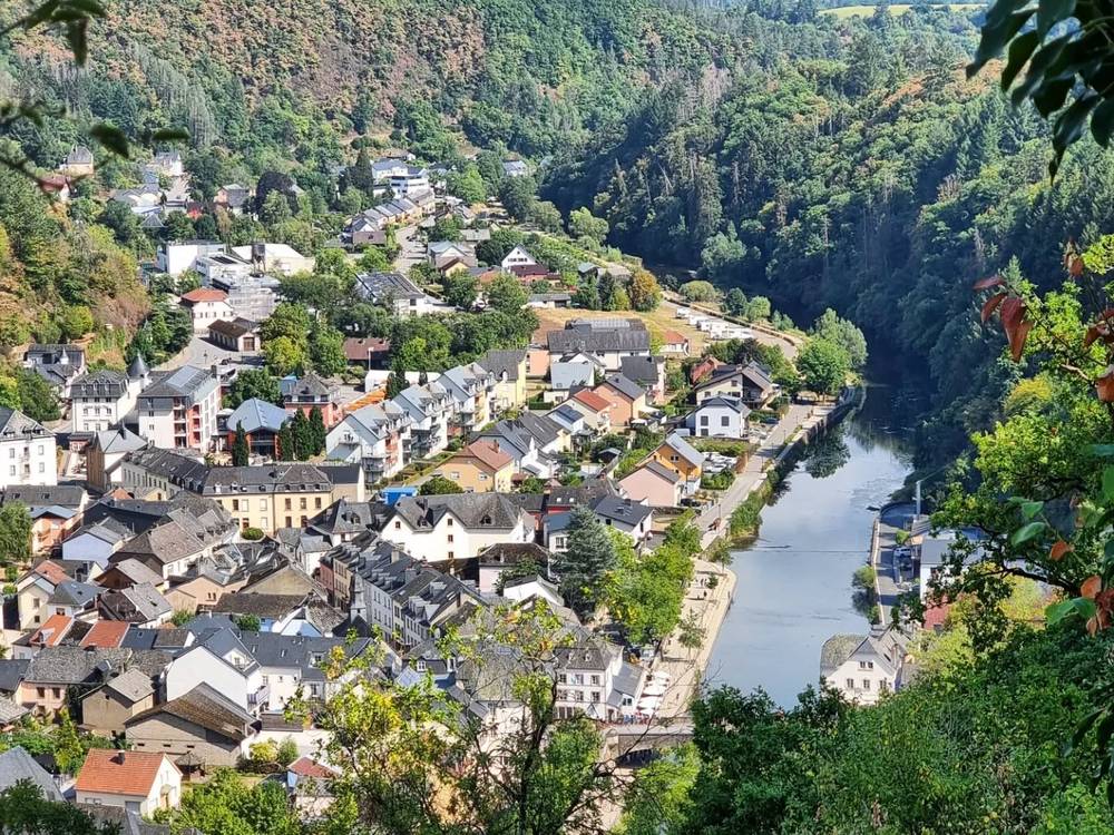 An aerial view of a small town nestled in a forested valley beside a winding river.