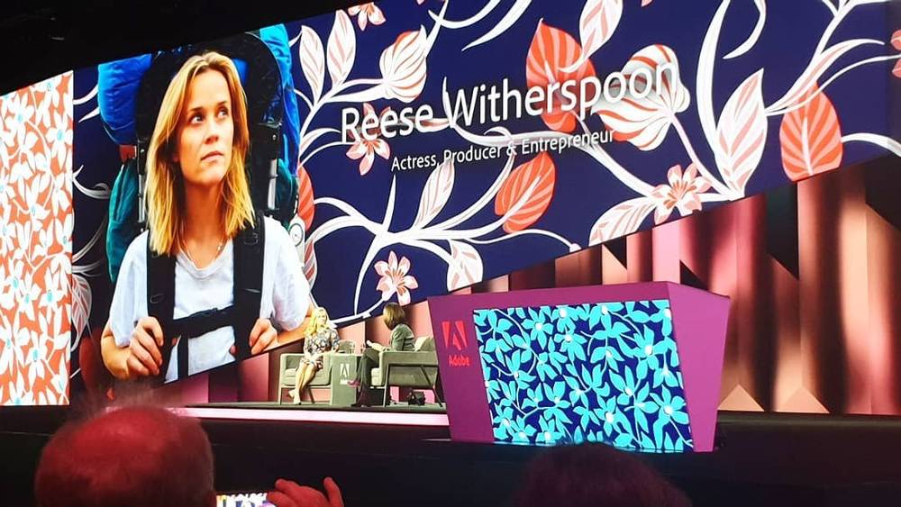 A large stage screen introduces "Reese Witherspoon, Actress, Producer & Entrepreneur" at a conference.
