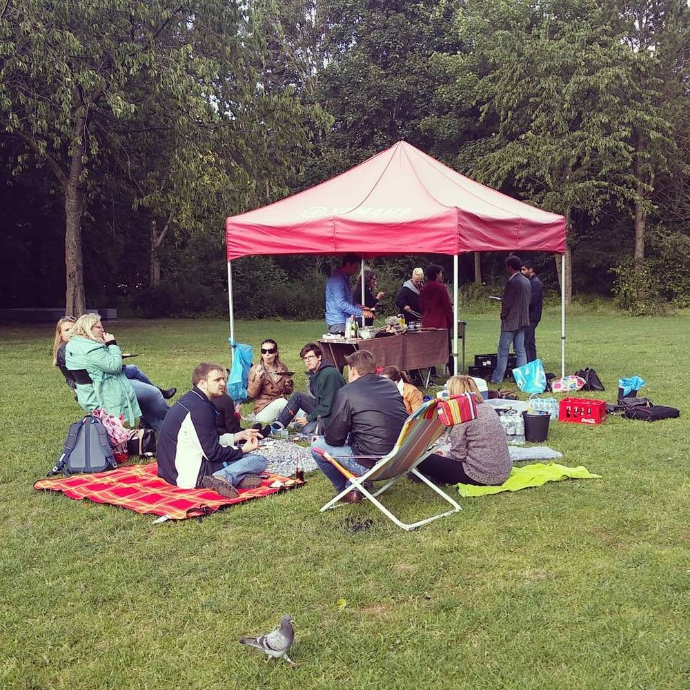 A group of people relax on picnic blankets under a pink tent canopy in a park.