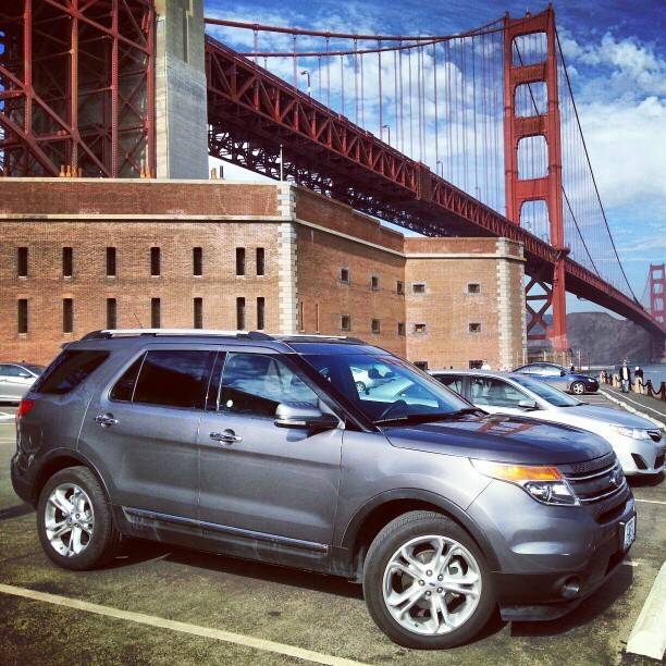 An SUV parked near a historic brick fort beneath the Golden Gate Bridge.