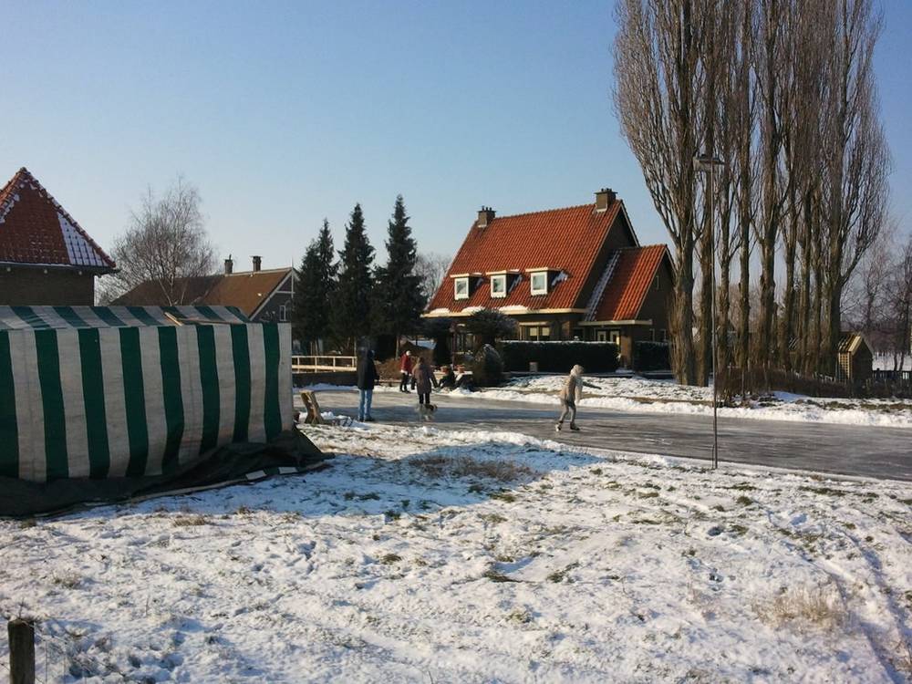 A striped refreshment tent stands beside a snow-covered path near old houses.