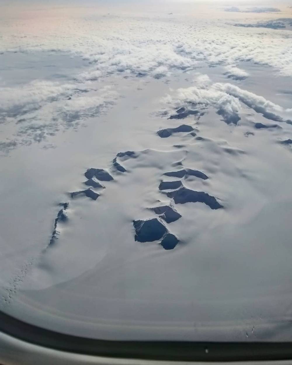 Aerial view of an icy, cracked landscape from an airplane window.