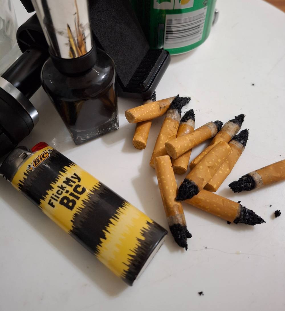 A pile of cork-filtered cigarettes and a yellow and black lighter.