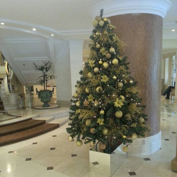 A decorated Christmas tree standing between marble columns in a grand hotel lobby.
