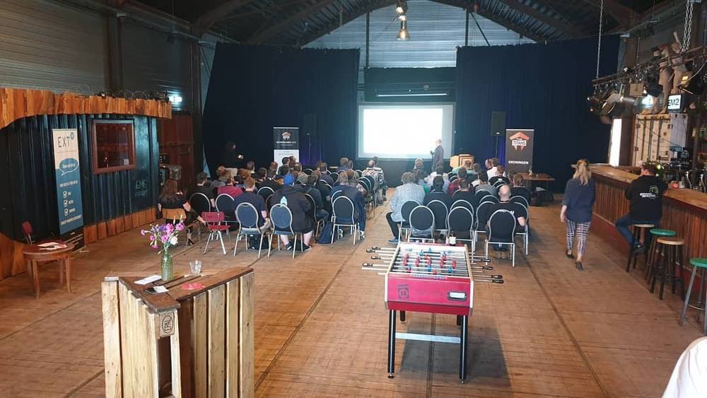 The interior of an event venue with rows of chairs facing a screen and a foosball table nearby.