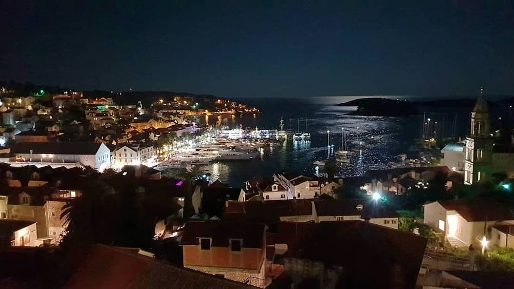 A harbor town lit up at night, boats moored along the waterfront.