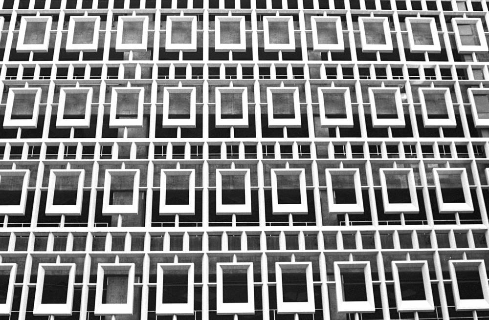 Abstract pattern of a brutalist office facade, a repeating grid of recessed square windows framed in pale concrete.