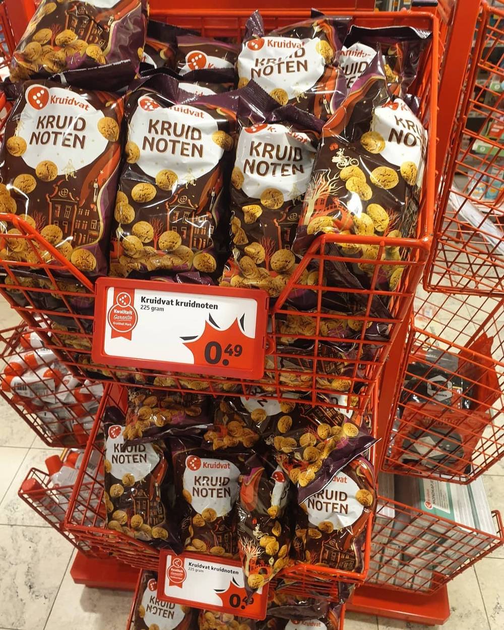 A shopping cart filled with bags of Kruidnoten at a Kruidvat store, priced 0.49 each.