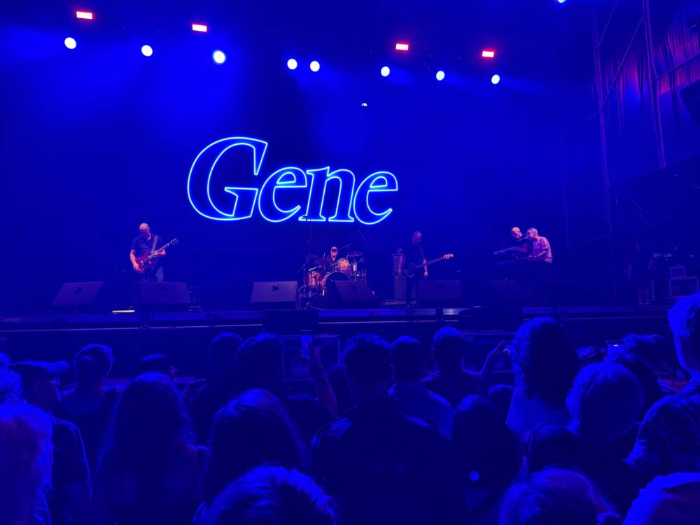 A band bathed in blue light: men playing guitar, drums, bass and keys. The band's name, Gene, in blue neon above them.