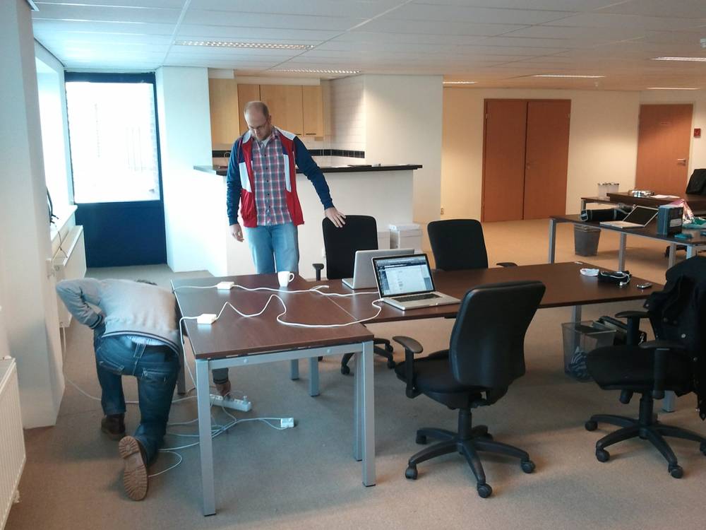 A man kneels to install cables under a desk in a mostly empty new office.