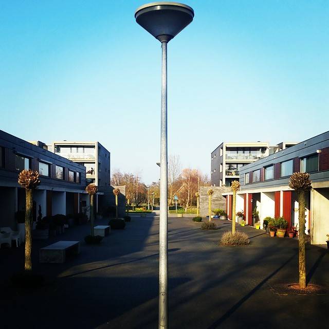 A tall lamppost stands in a paved courtyard between modern townhouses under a blue sky.