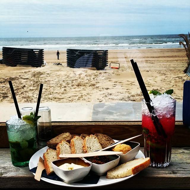 Two iced cocktails and a bread basket on a table overlooking a sandy beach.