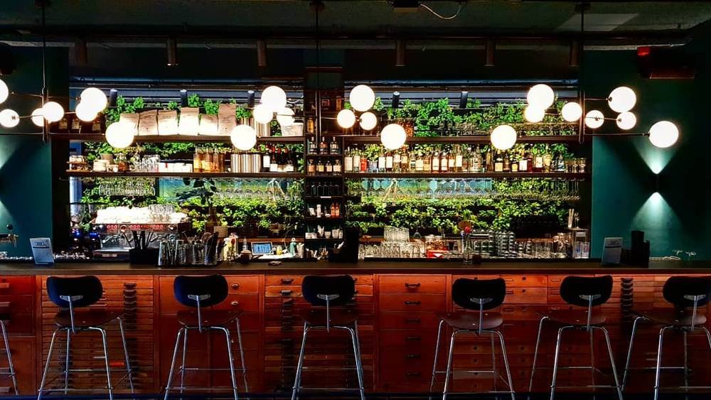 An empty bar with shelves of bottles and hanging lights.