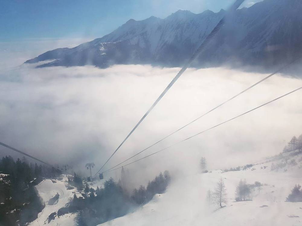 A cable car's cables extending down through mountain fog into a valley below.