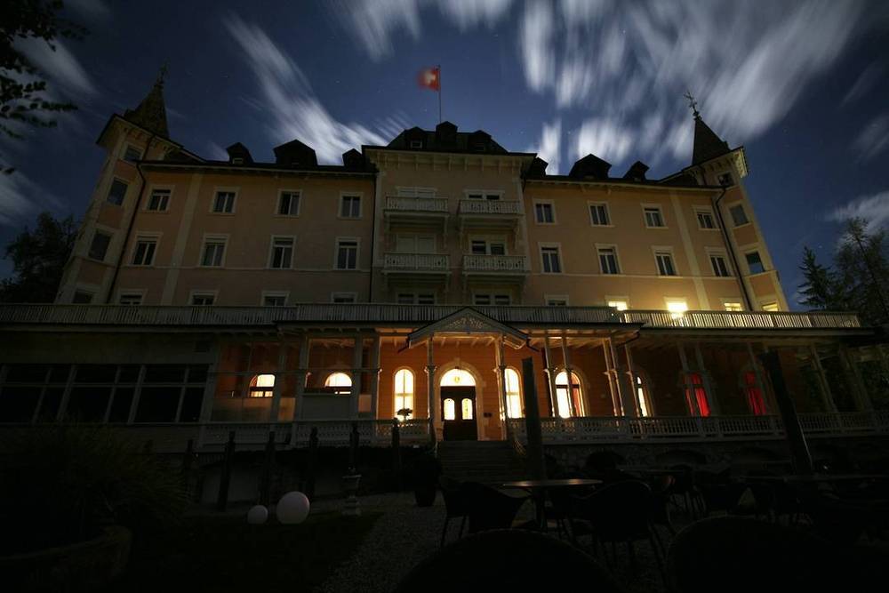 A grand European hotel building lit up at night under a cloudy sky.