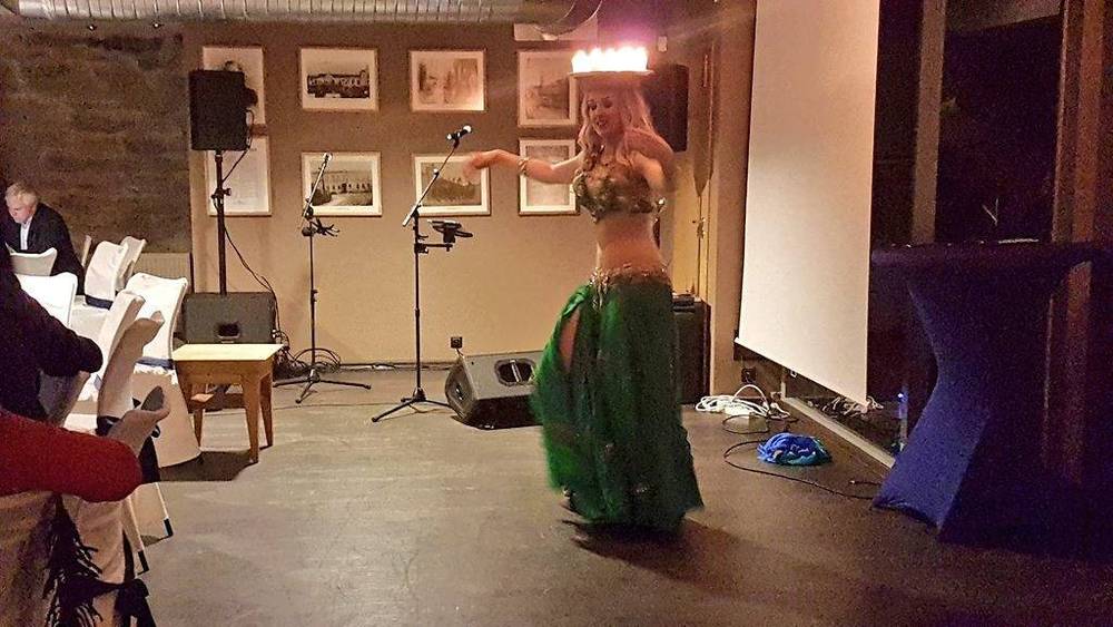A belly dancer performing on a small stage in front of a seated audience.