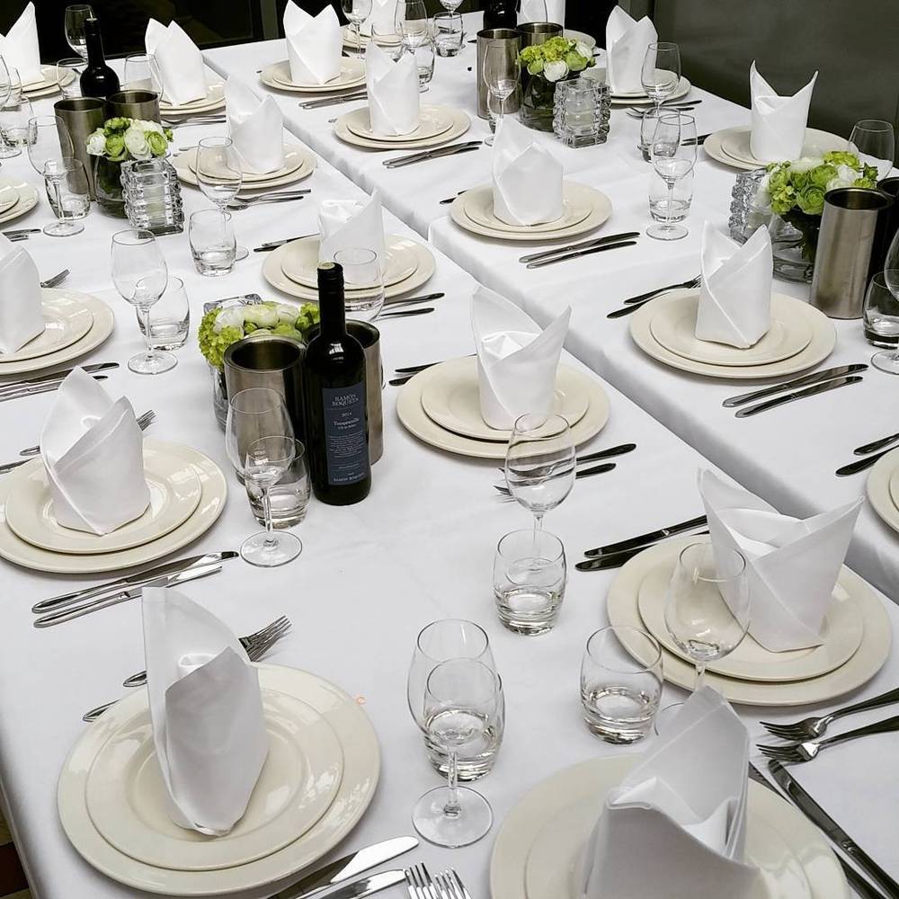A long table set for a formal dinner with white linens, folded napkins, wine glasses and small flower arrangements.