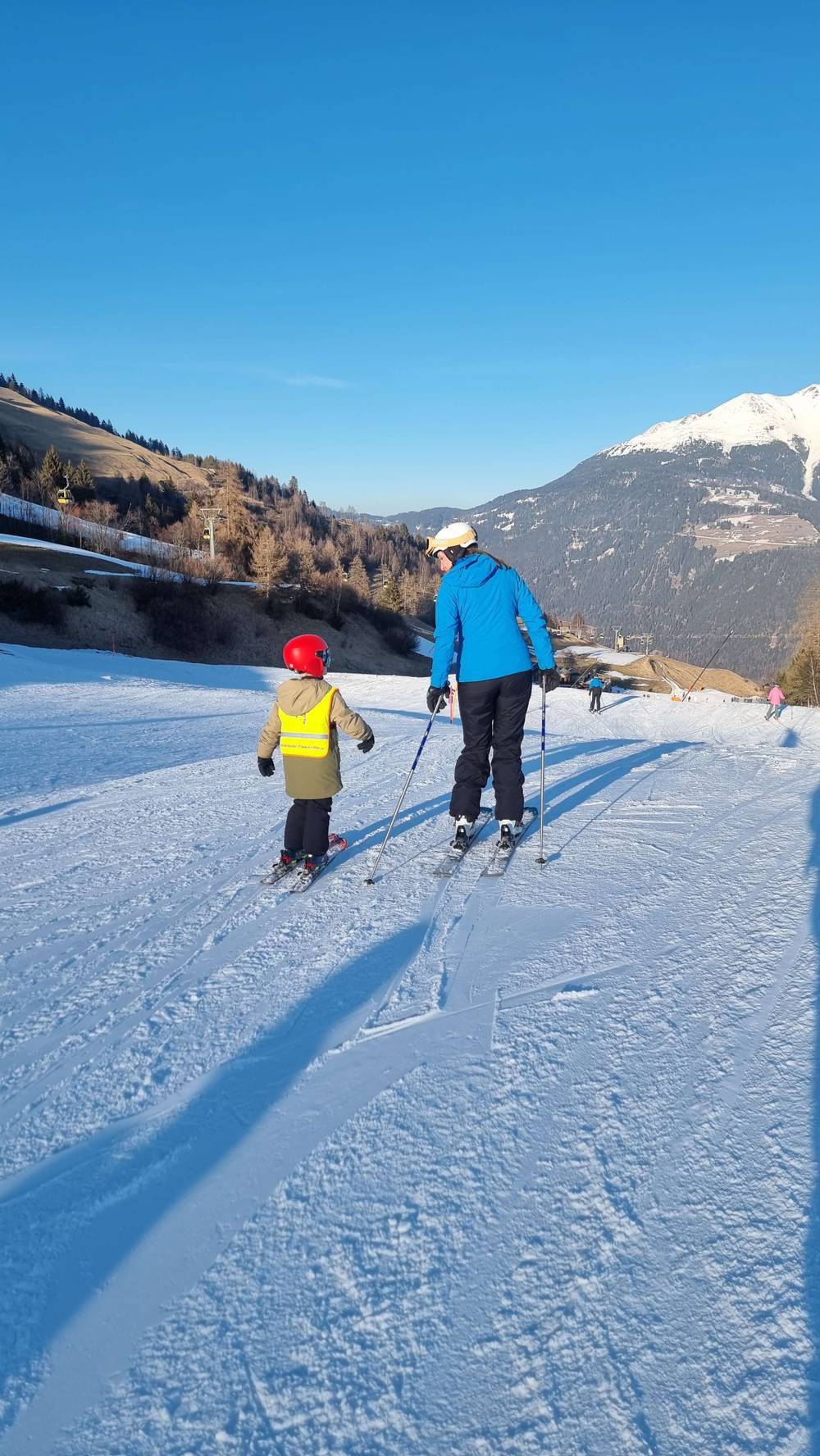 Two skiers, one adult and one child, ski down a snowy slope.