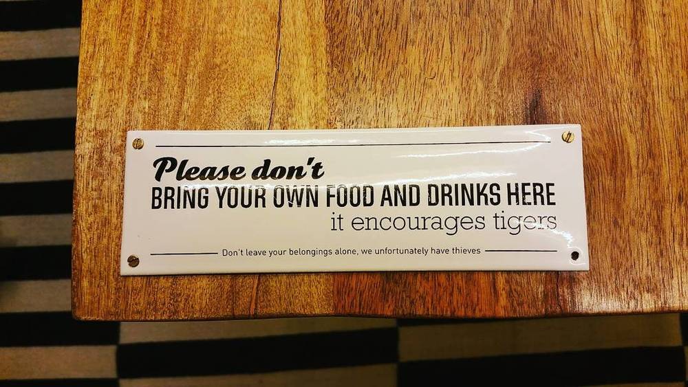 A wooden sign reading "Please don't bring your own food and drinks here, it encourages tigers."