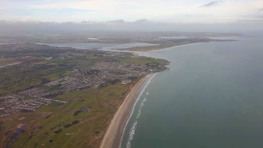 Aerial view of a coastline curving away with beach, fields and a bay.