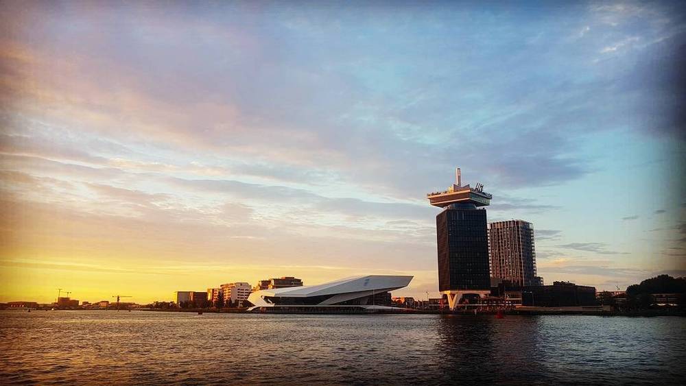 Sunset over the water in Amsterdam, with the A'DAM Tower and EYE Film Museum silhouetted against the sky.