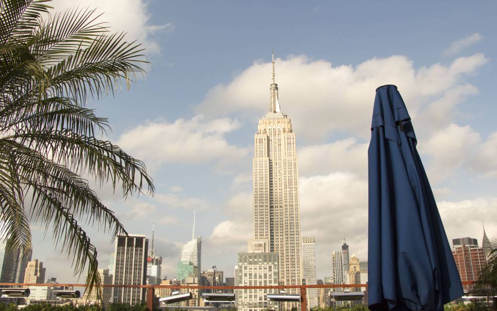 The Empire State Building rises beyond palm plants on a rooftop terrace.