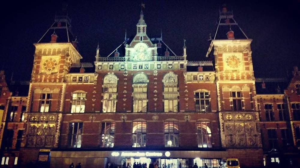 The illuminated facade of Amsterdam Centraal railway station at night.