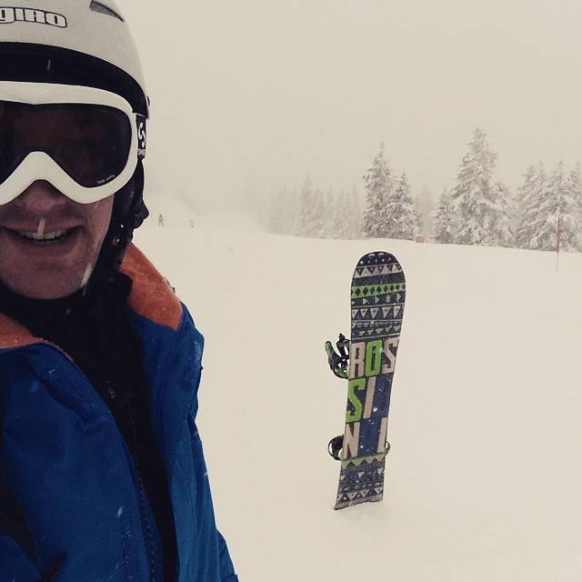 A snowboarder descends a slope with mountains and a chairlift in the background.