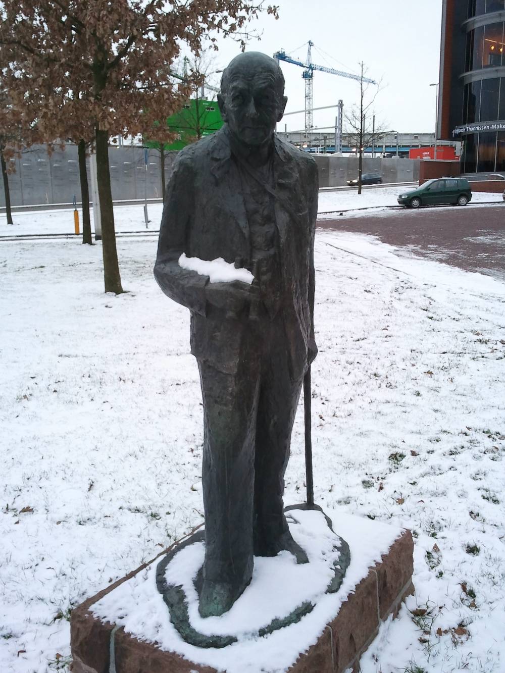 A bronze statue of a man stands in a snow-covered park.