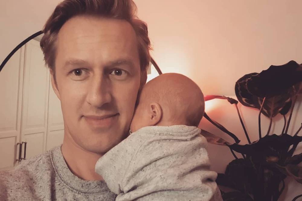 Close selfie of a man with a baby's head resting against his cheek.