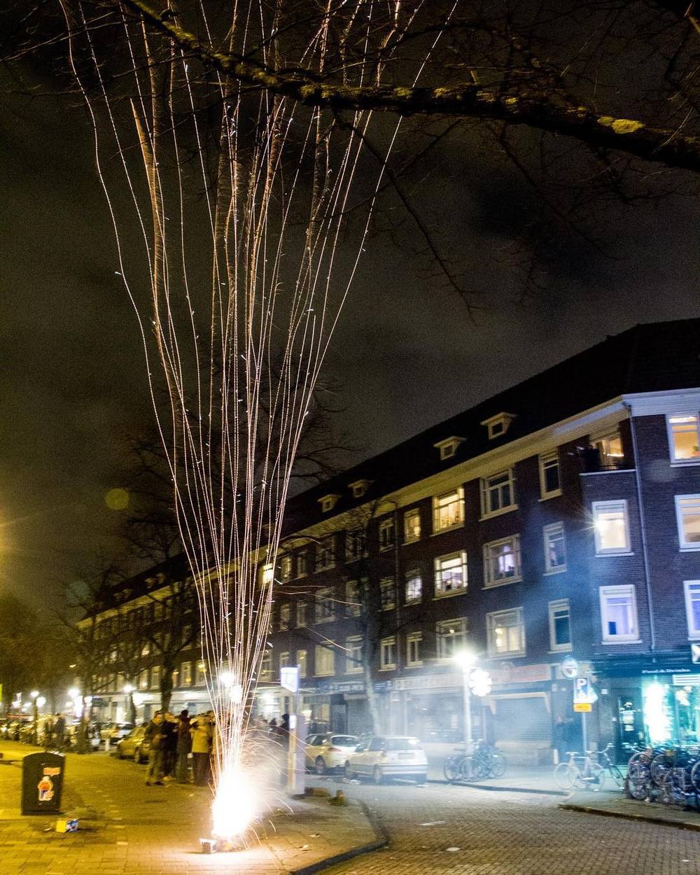 Sparks trailing from a firework display on a residential street at night.