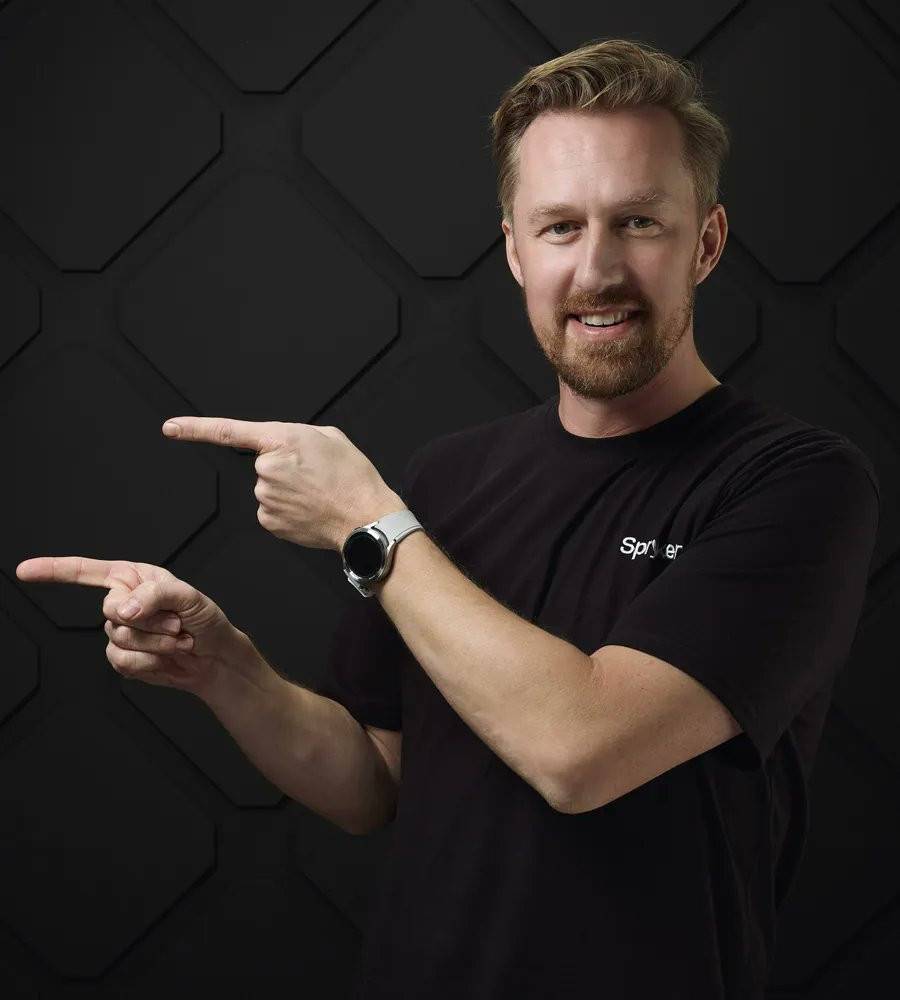 A studio portrait of a man in a Spryker t-shirt pointing to the side.